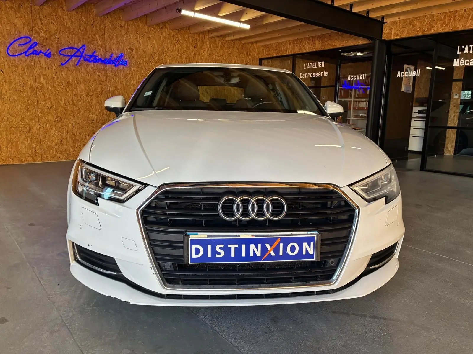 Vue de face d'une Audi A3 Sportback blanche 2019 avec calandre noire et logo Audi visible en intérieur showroom.