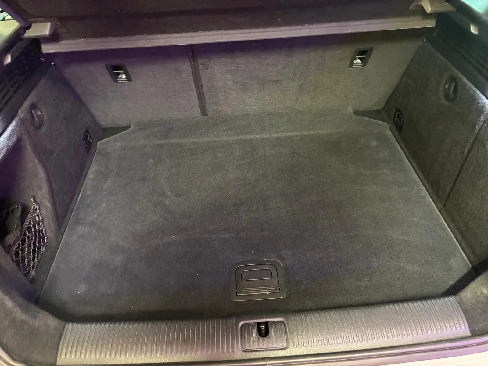 Coffre vide en vue plongeante d'une Audi A3 Sportback blanche, montrant le revêtement intérieur noir et les rangements latéraux.