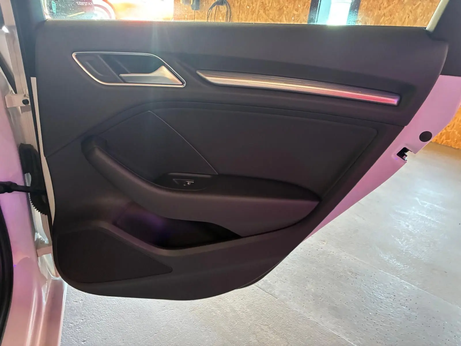 Vue intérieure de la porte arrière gauche noire d'une Audi A3 Sportback blanche, avec poignée et commande de fenêtre.