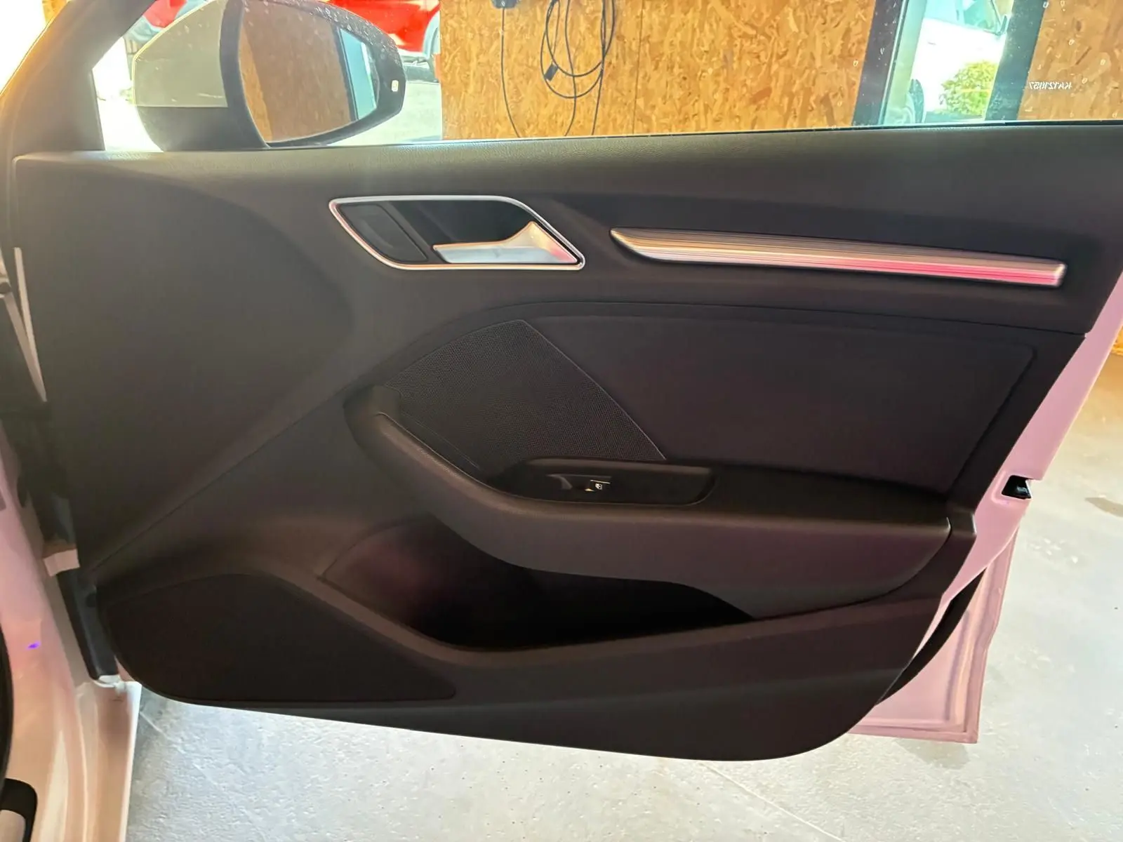 Vue intérieure de la porte avant gauche noire de l'Audi A3 Sportback blanche, avec poignée et commande de fenêtre.