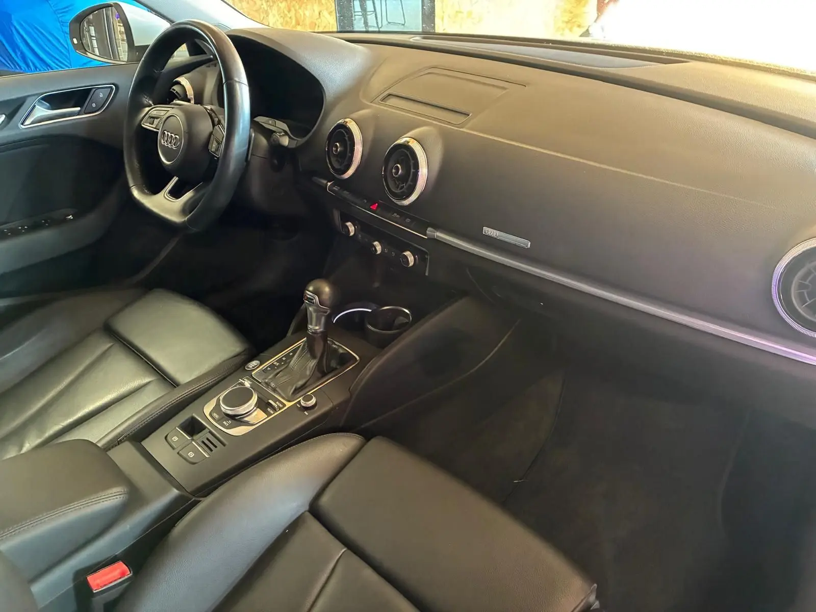 Vue intérieure côté conducteur de l'Audi A3 Sportback 2019, tableau de bord noir avec volant et console centrale en cuir.