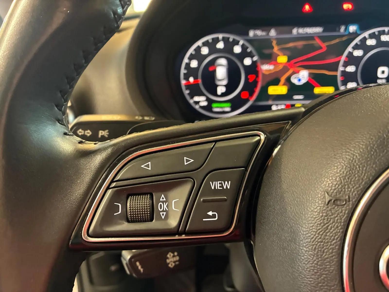 Gros plan sur les commandes au volant côté gauche de l'Audi A3 Sportback blanc avec tableau de bord numérique en arrière-plan.