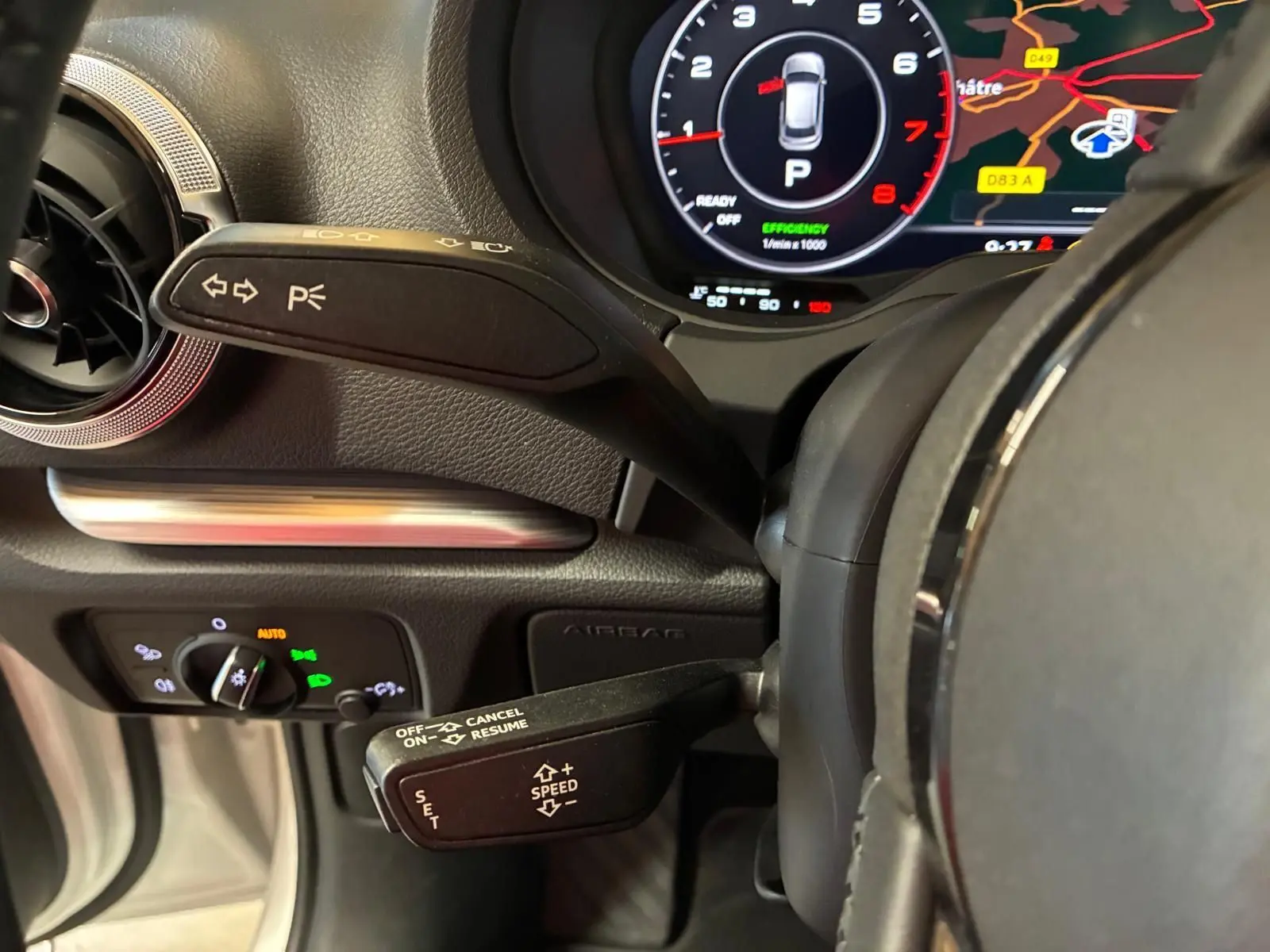 Gros plan sur le volant et le combiné d'instruments numérique d'une Audi A3 Sportback blanche, affichant la navigation et les commandes au volant.