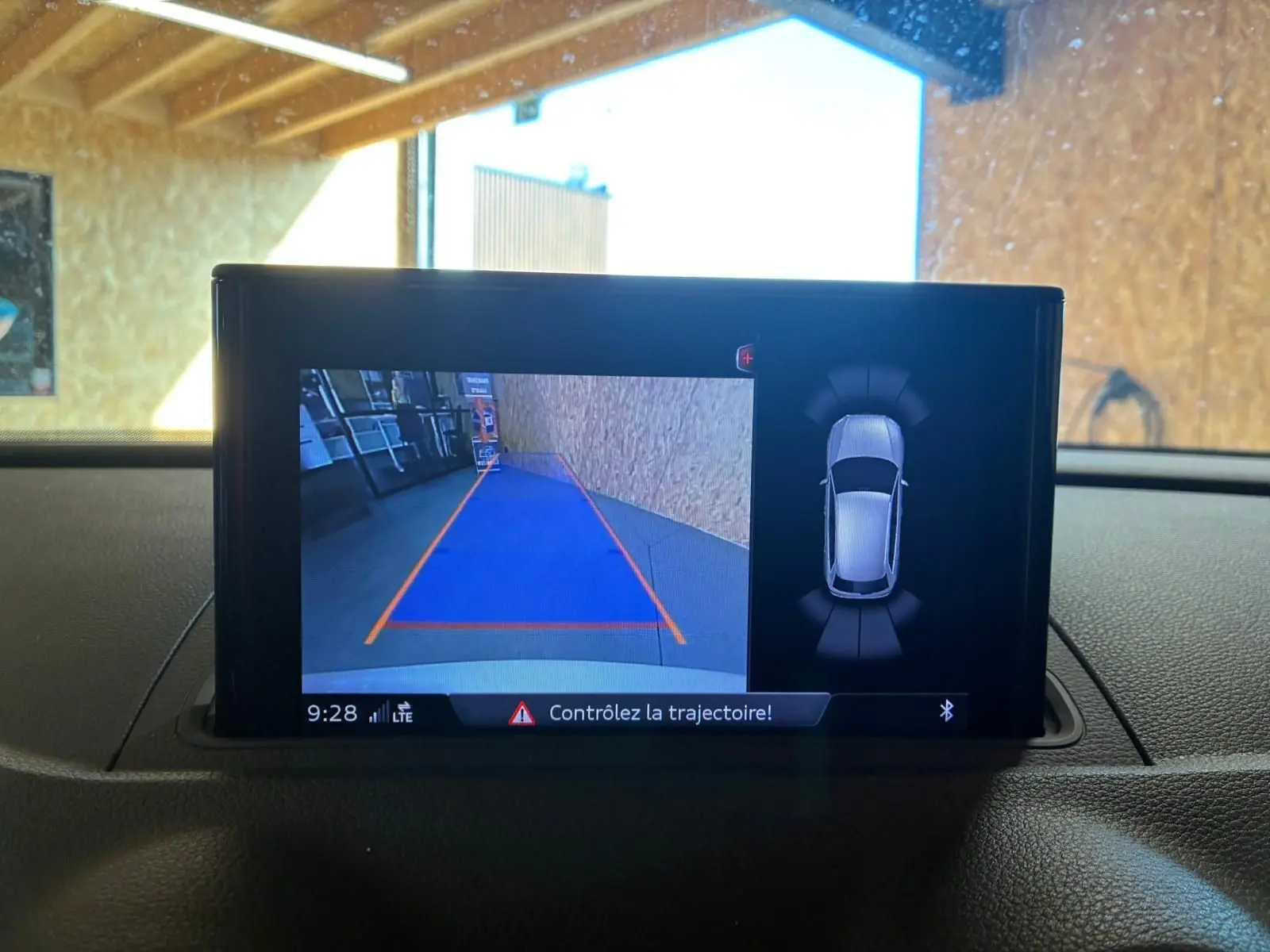 Écran central de l’Audi A3 Sportback blanc montrant la caméra de recul avec guidage de trajectoire et vue 360° du véhicule.