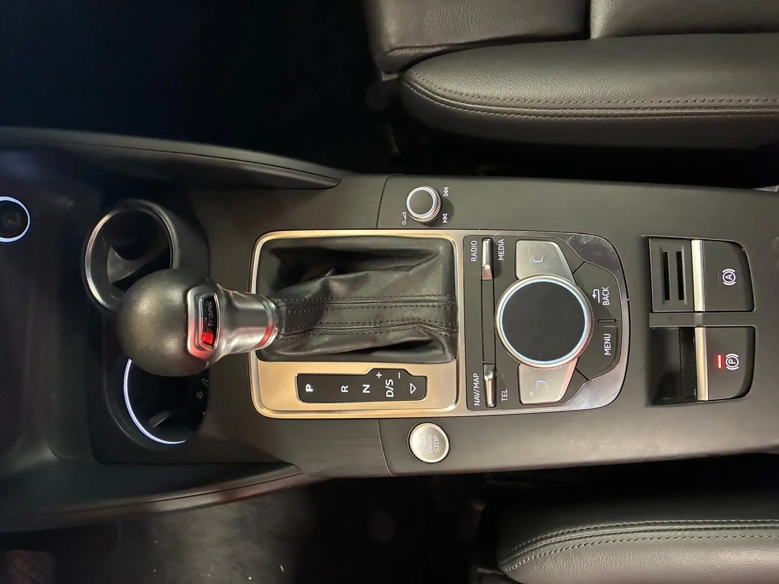 Vue rapprochée du levier de vitesses automatique et du système de commande multimédia sur la console centrale noire d’une Audi A3 Sportback blanche.
