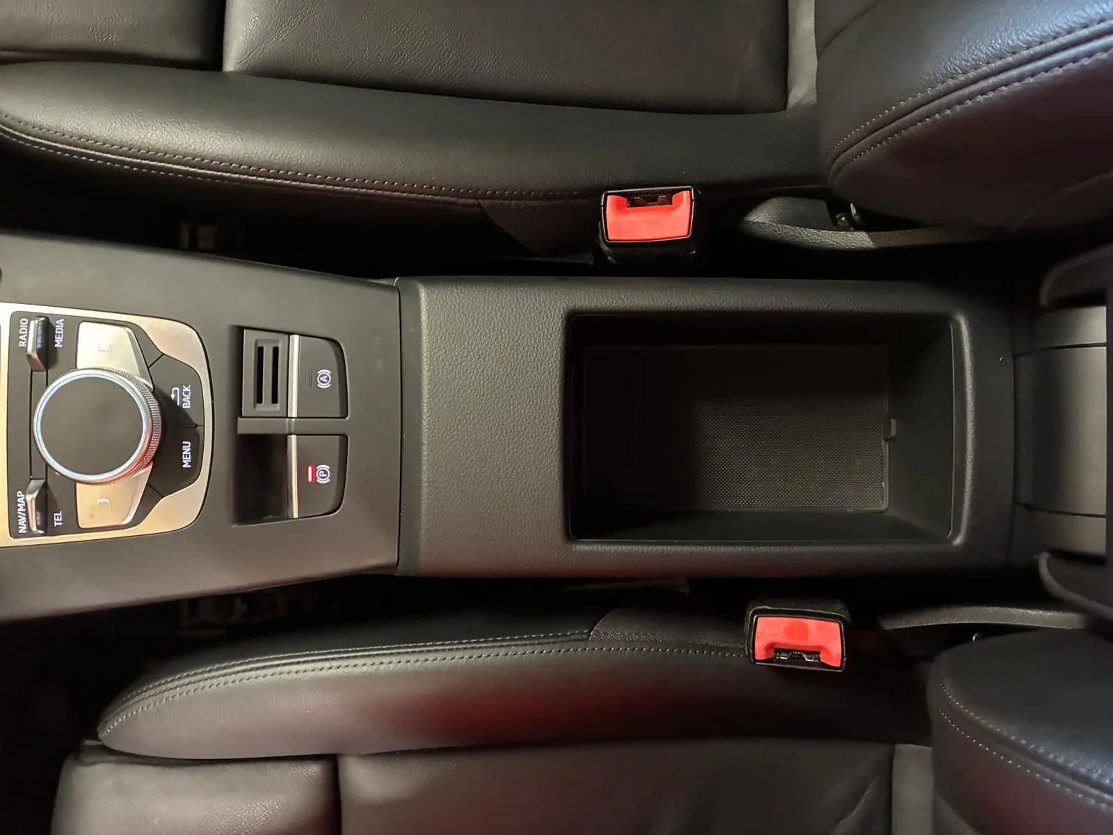 Vue plongeante sur la console centrale noire en cuir de l'Audi A3 Sportback, avec commandes multimédia et ceintures rouges.
