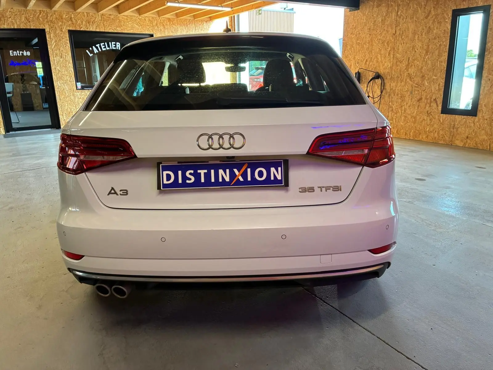 Vue arrière d'une Audi A3 Sportback blanche 35 TFSI avec double sortie d'échappement, stationnée en intérieur.