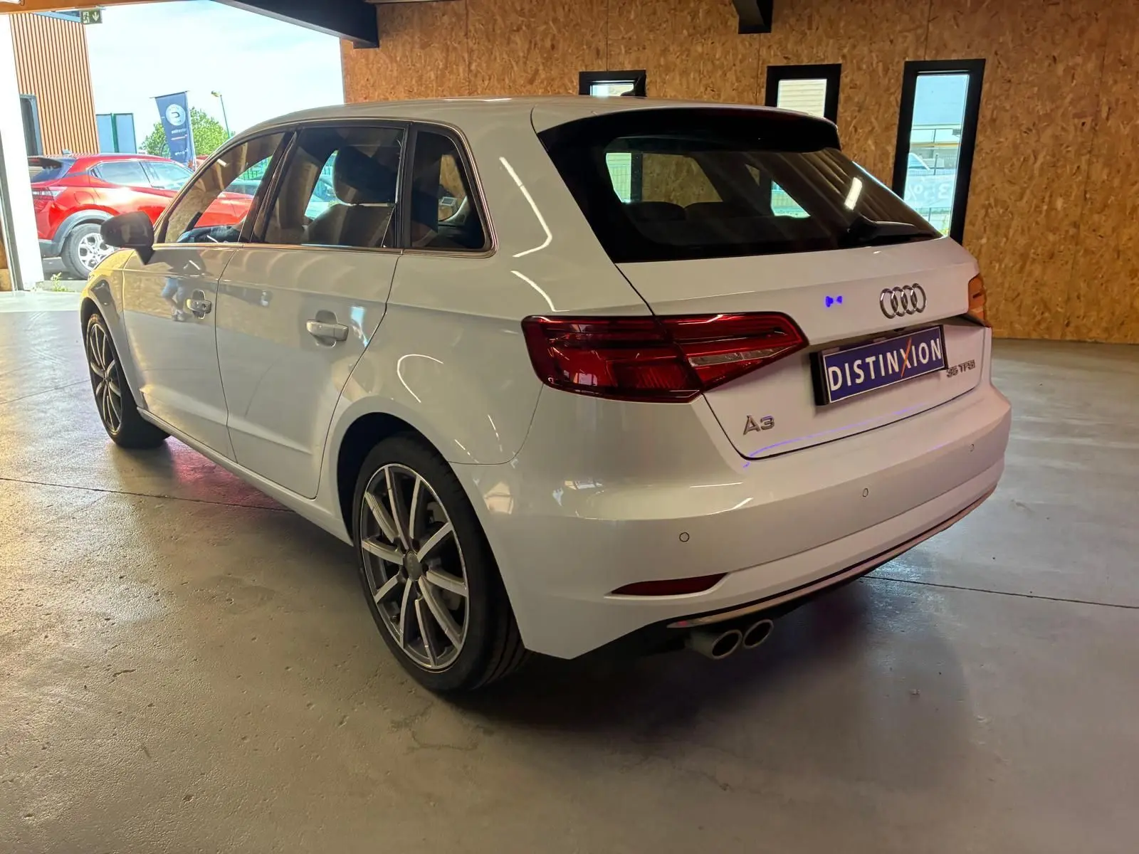 Audi A3 Sportback blanc vue 3/4 arrière droit en intérieur, avec jantes alliage et double sortie d’échappement.