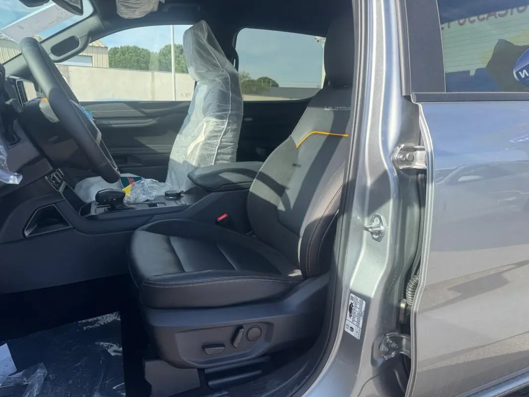 Vue intérieure côté conducteur du Ford Ranger gris 2025, siège Wildtrak avec surpiqûres orange et accoudoir central.