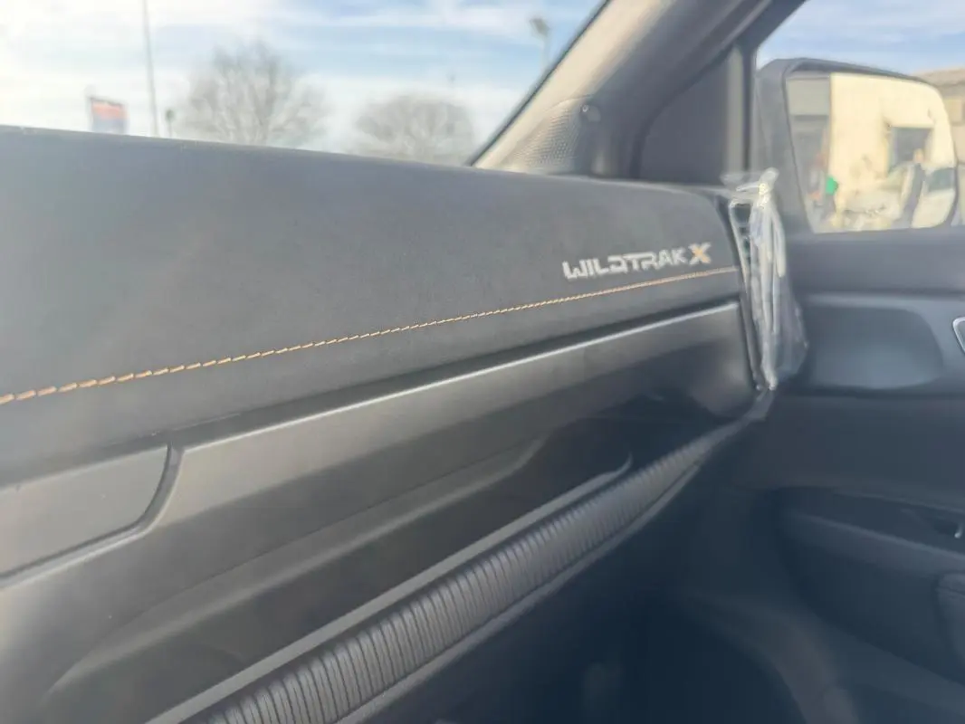 Vue intérieure côté passager du tableau de bord noir avec logo Wildtrak X et surpiqûres orange du Ford Ranger gris 2025.