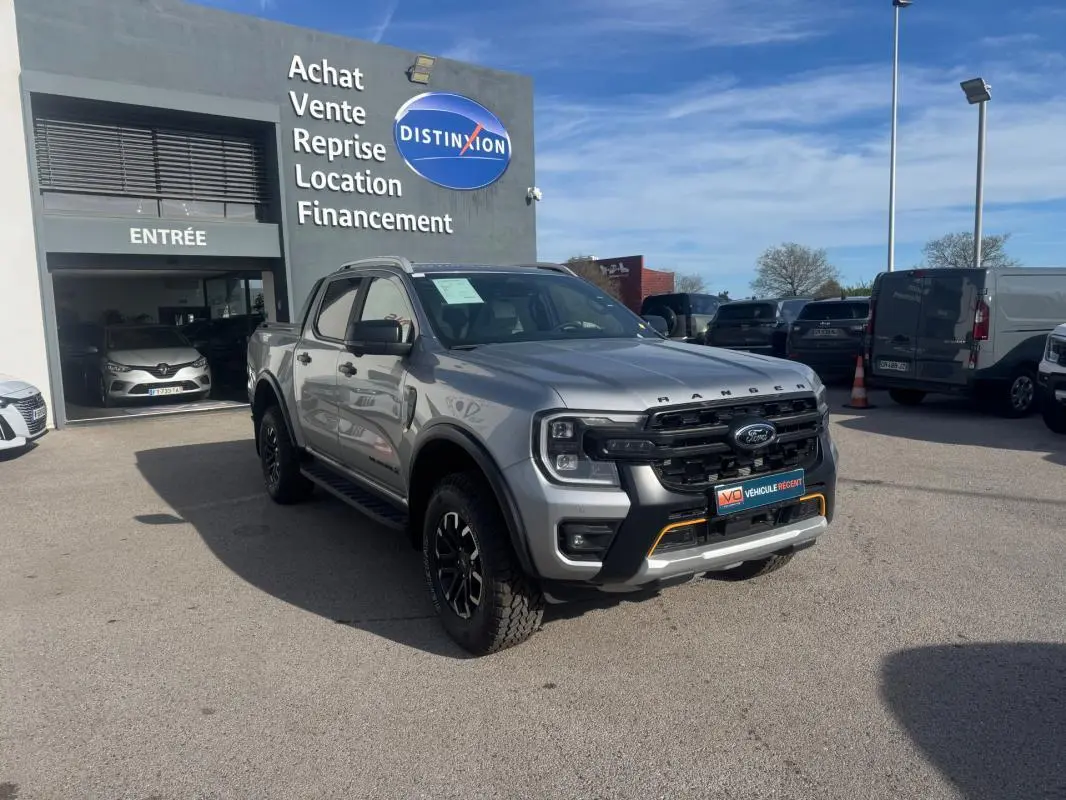Ford Ranger Wildtrak gris en 3/4 avant droit, avec jantes alliage noires et barres de toit visibles.