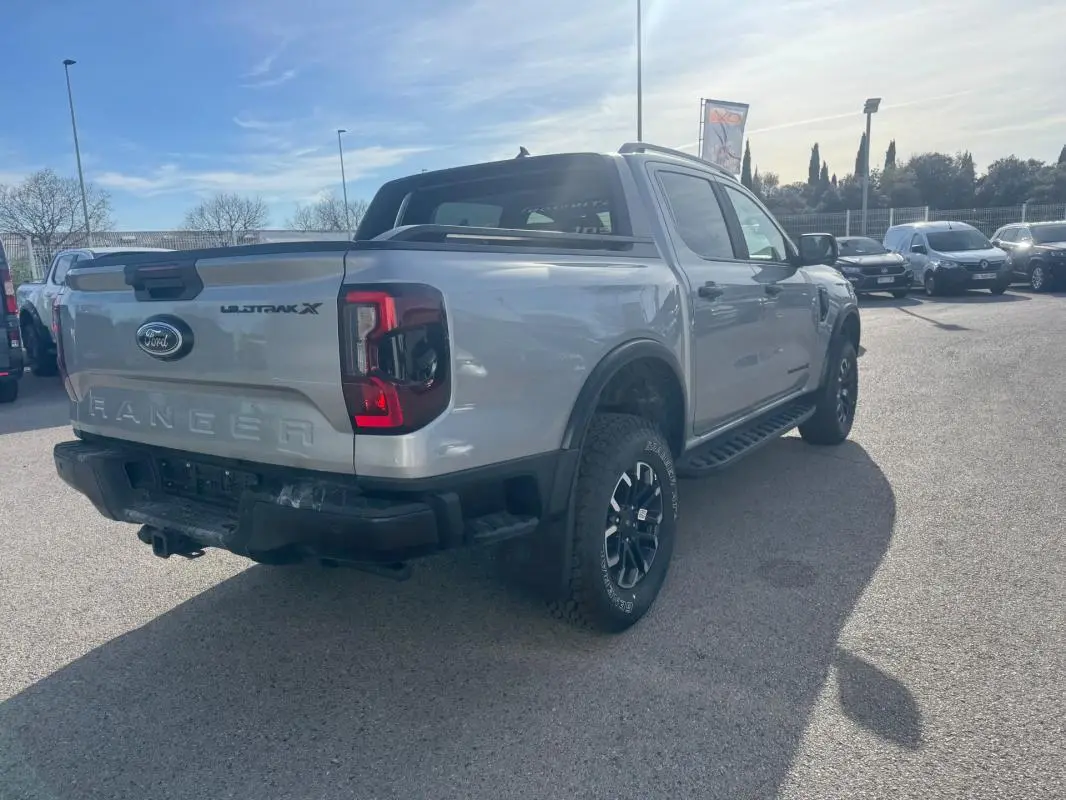 Vue 3/4 arrière droite d'un Ford Ranger gris 2025 Wildtrak X avec jantes alliage noires et barres de toit.