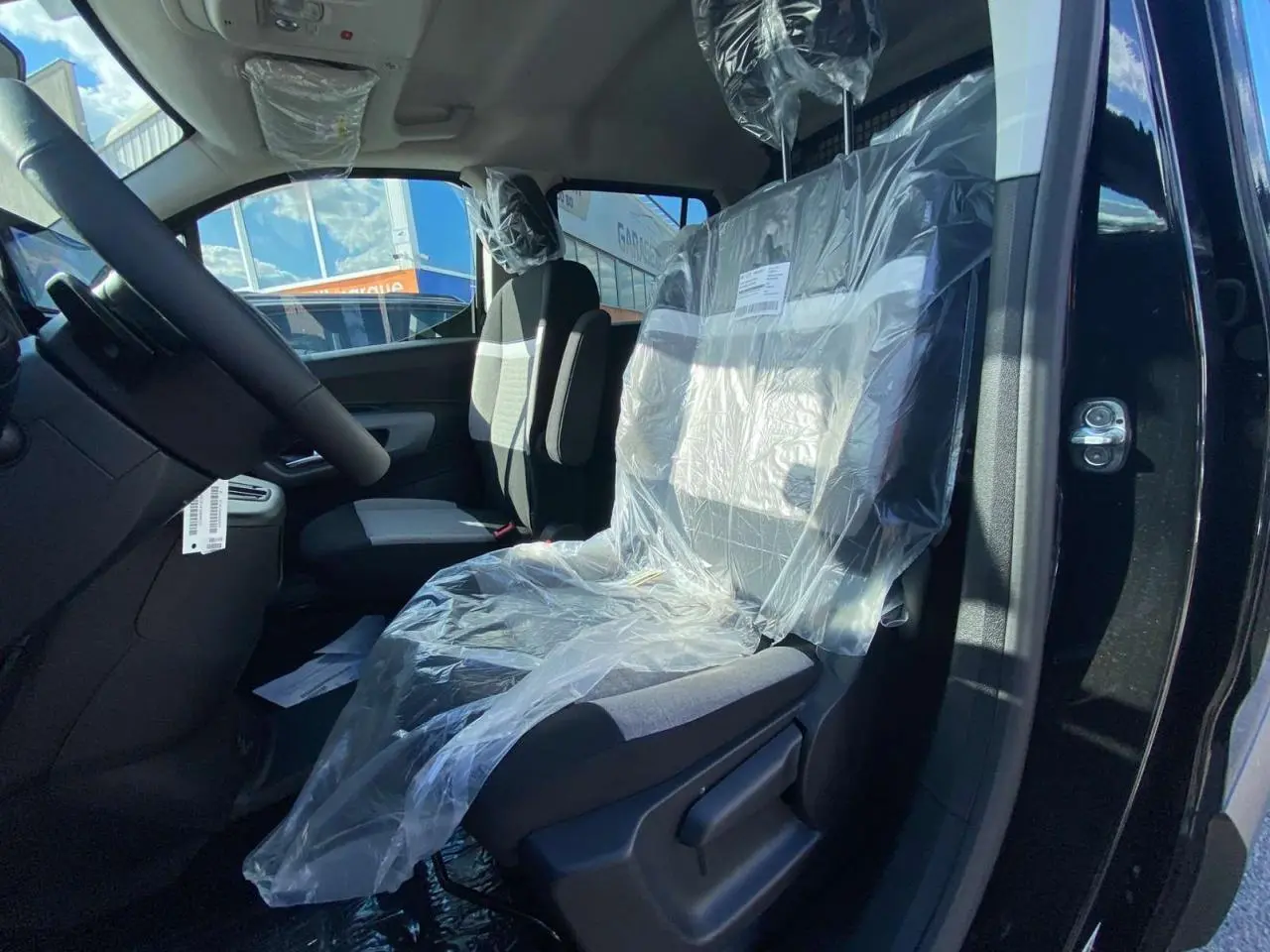 Vue intérieure côté conducteur du Citroën Berlingo noir 2026, sièges avant protégés par film plastique.