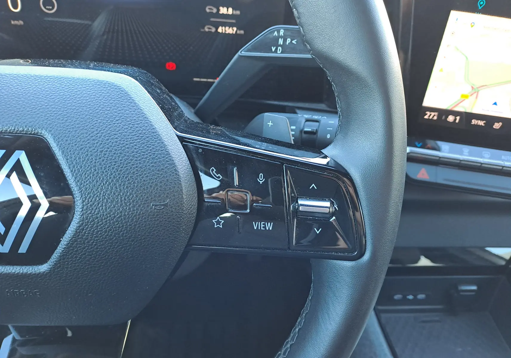 Vue rapprochée du volant noir du Renault Austral gris schiste 2023, avec commandes intégrées et écran tactile visible en arrière-plan.