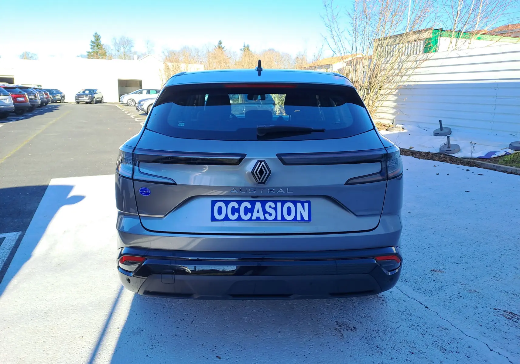 Vue arrière d'un Renault Austral gris schiste 2023 avec logo distinctif et plaque "OCCASION" sur parking extérieur.