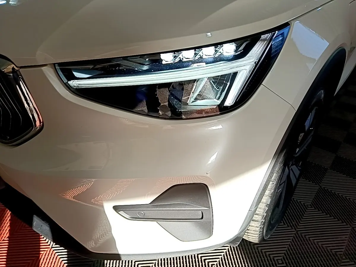 Gros plan sur le phare avant droit d’un Volvo XC40 Recharge T5 262 DCT7 Plus beige avec détails LED et partie de la roue.