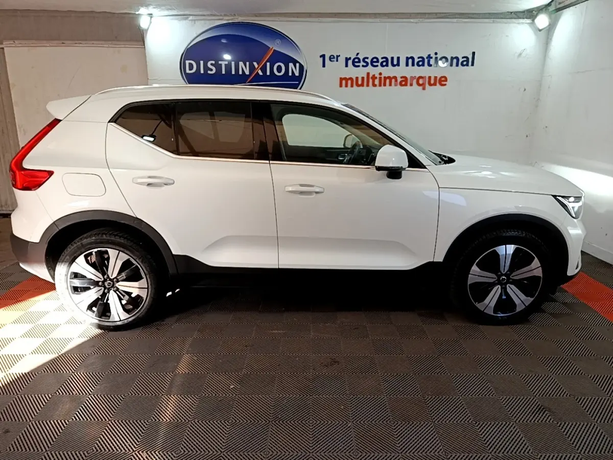 Vue de profil côté droit d'un Volvo XC40 Recharge T5 blanc, avec jantes spécifiques et toit blanc dans un showroom.