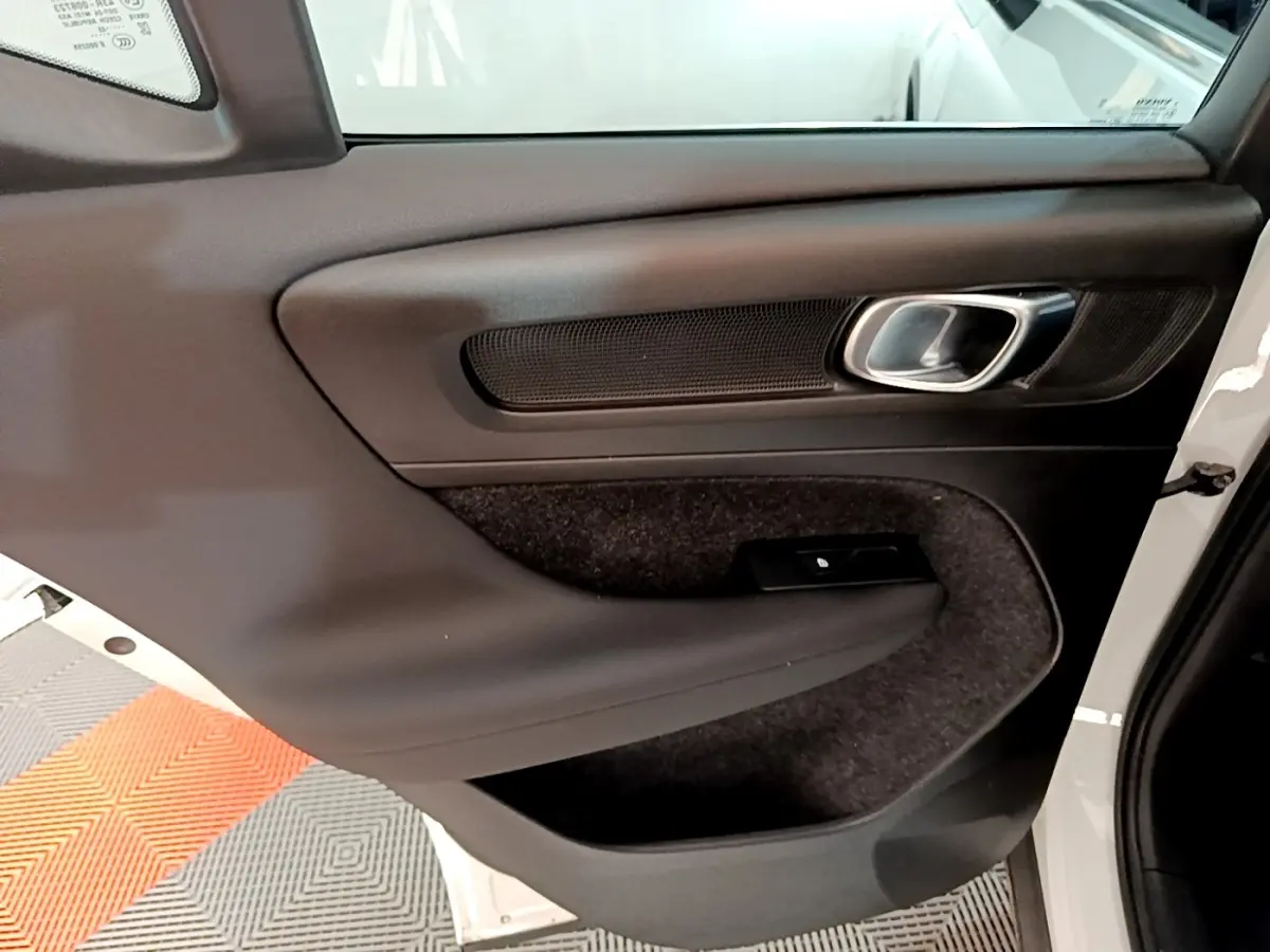 Vue intérieure côté gauche de la porte avant d’un Volvo XC40 Recharge T5 262 DCT7 Plus avec garniture noire et poignée métallique.