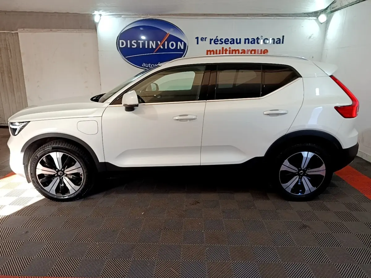 Vue latérale droite d'un Volvo XC40 hybride rechargeable blanc avec jantes noires et grises, dans un showroom.