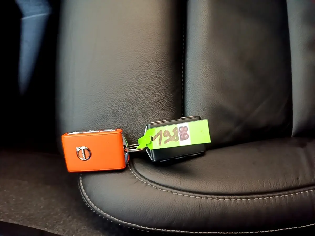 Clé orange Volvo posée sur siège en cuir noir à couture apparente, vue rapprochée intérieure du véhicule.