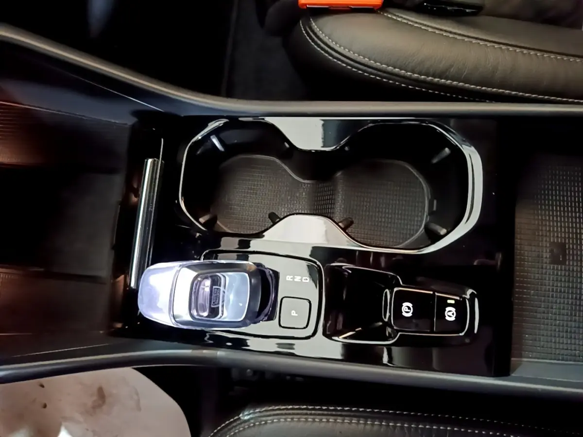 Vue plongeante sur la console centrale noire brillante du Volvo XC40 Recharge T5 avec levier de vitesses cristal et porte-gobelets.