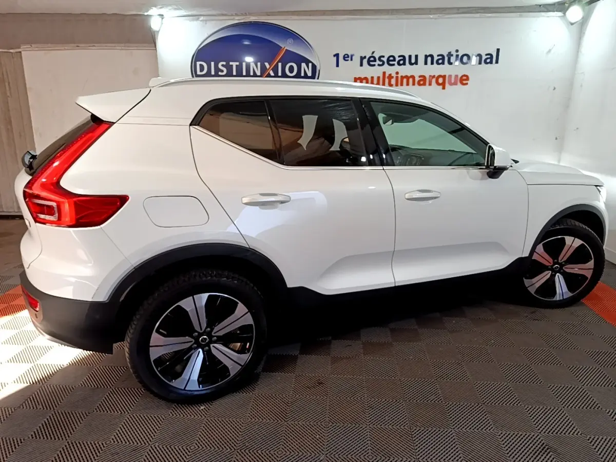 Vue de profil côté droit d'un Volvo XC40 Recharge T5 blanc avec jantes noires et rouges, stationné en intérieur.