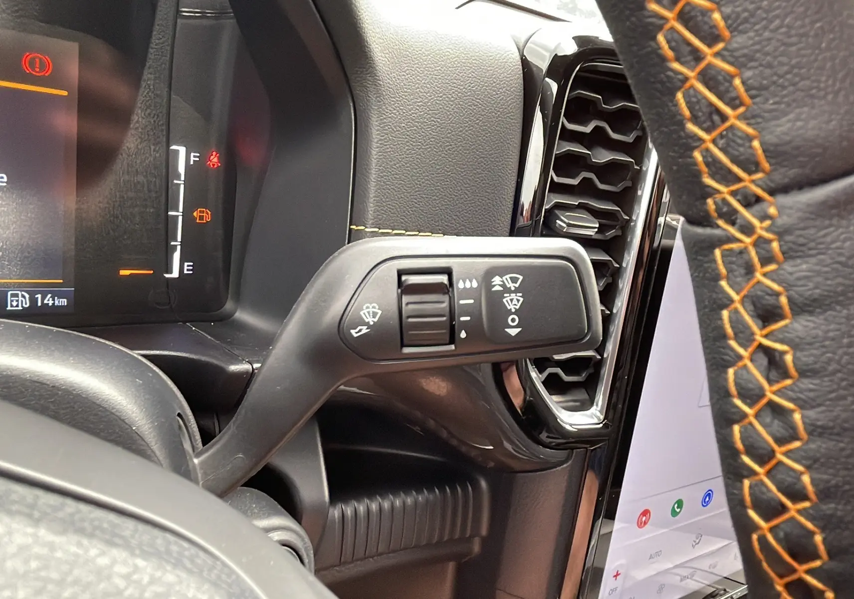 Gros plan sur la manette d’essuie-glace à gauche du volant cuir noir avec surpiqûres orange du Ford Ranger gris carbone.