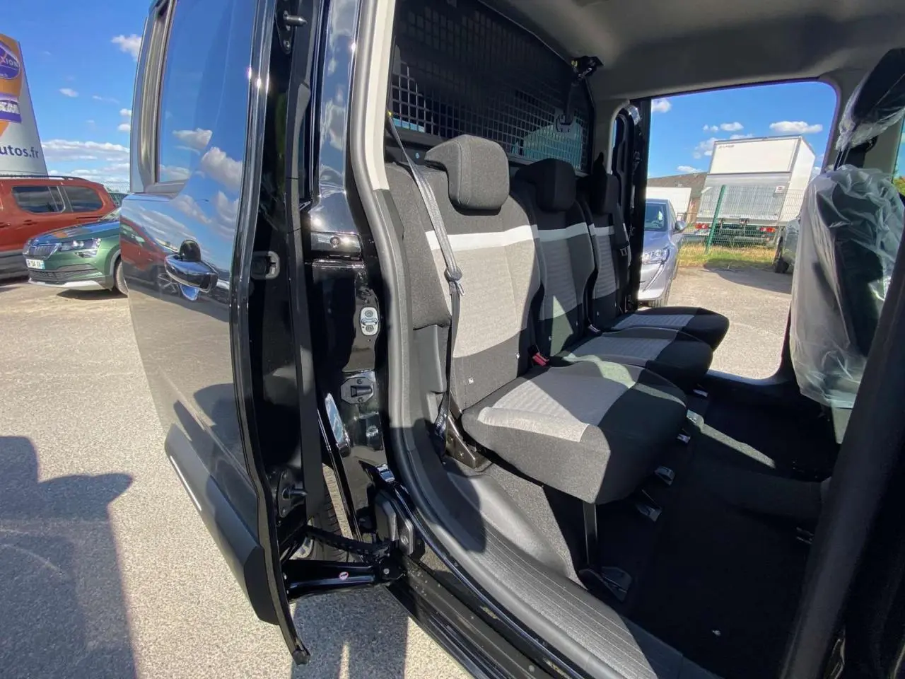 Vue latérale du Citroën Berlingo noir 2026 avec portes coulissantes ouvertes montrant les sièges arrière en tissu bicolore.