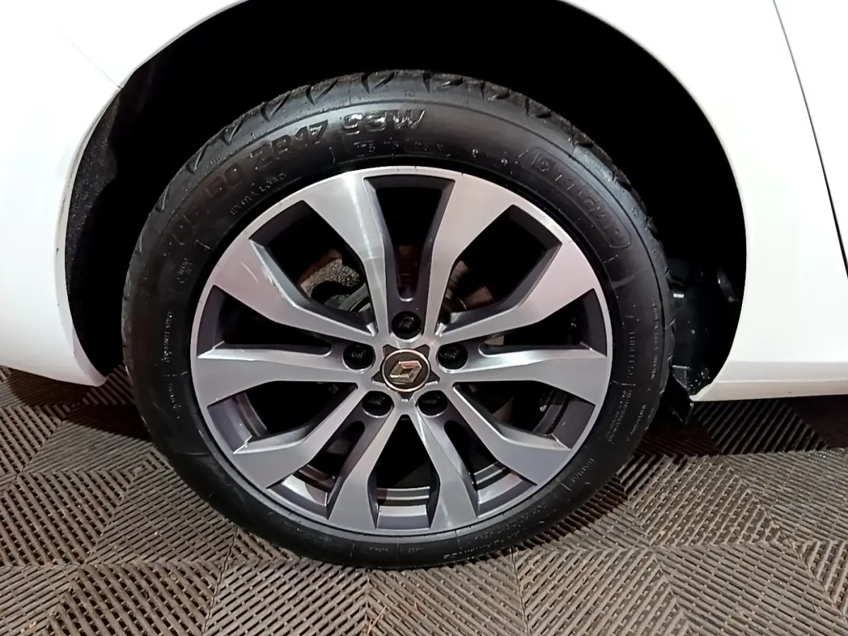 Gros plan sur la roue avant droite de la Renault Mégane blanche 2023 avec jante alliage gris et logo Renault central.