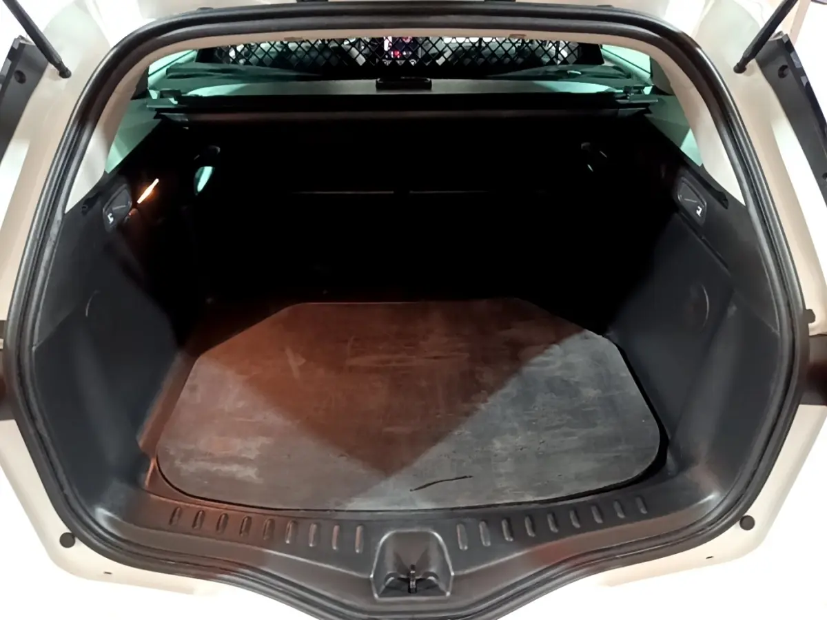 Coffre ouvert vu de l'arrière d'une Renault Mégane blanche 2023, espace de chargement vide avec tapis noir.