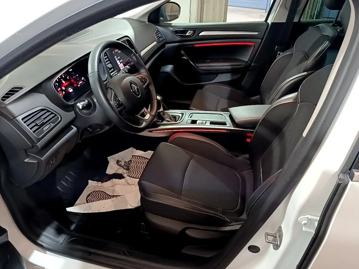 Vue intérieure côté conducteur de la Renault Mégane Techno TCe 140 blanche, avec tableau de bord et sièges noirs.