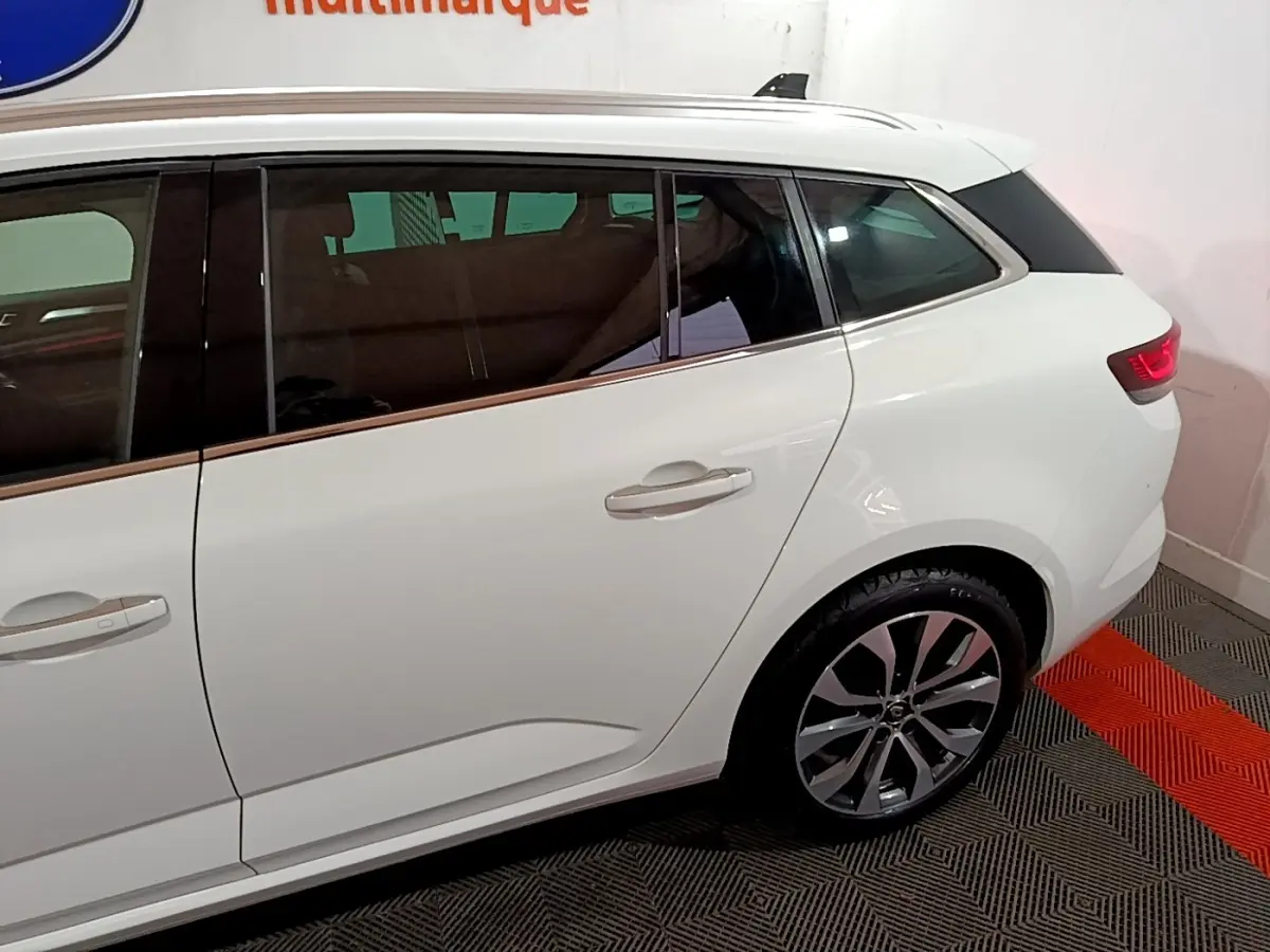 Vue latérale droite d'une Renault Mégane blanche, mettant en valeur la porte arrière et la roue arrière avec jante design.