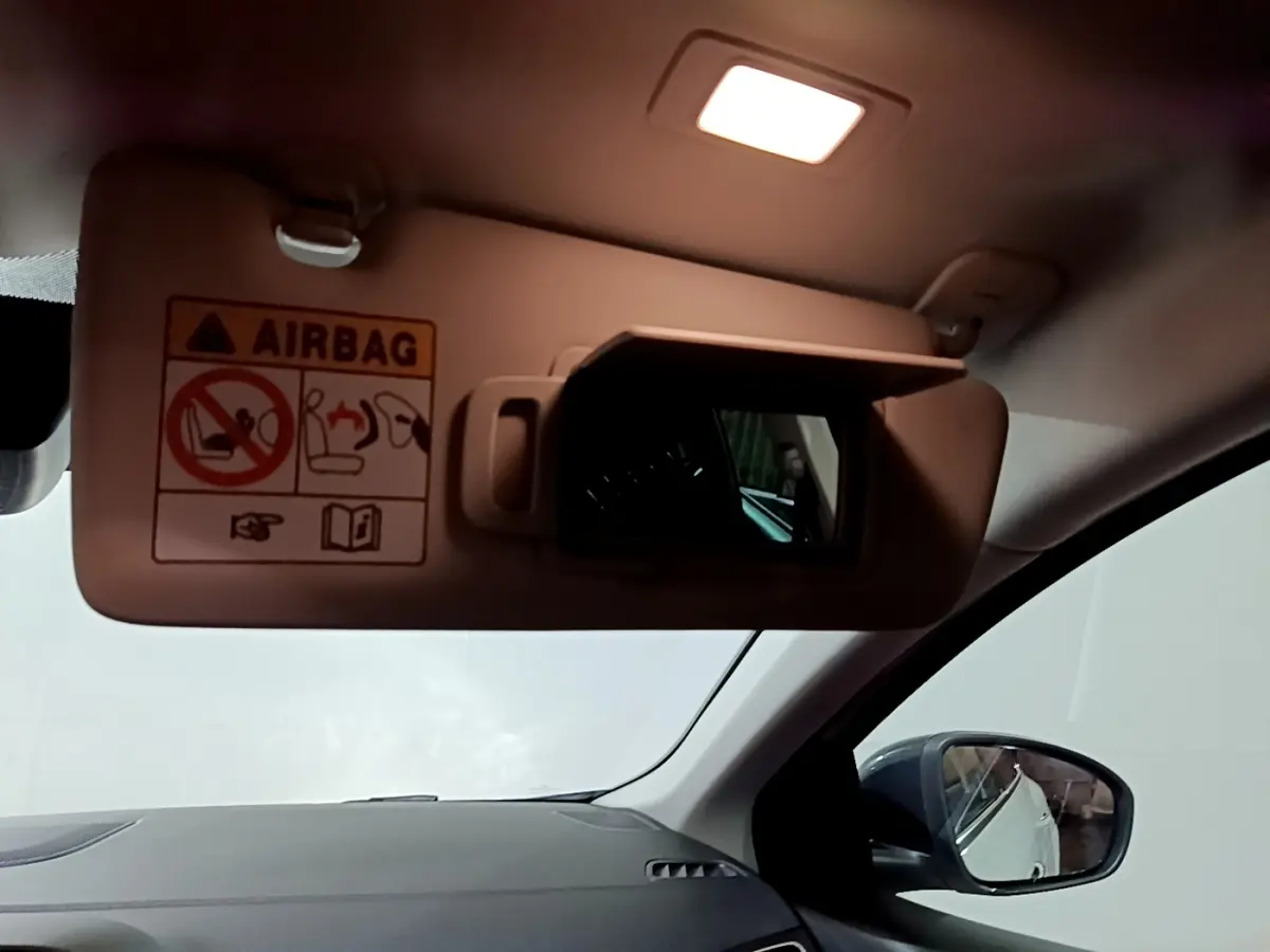 Vue intérieure du pare-soleil côté conducteur avec miroir et avertissement airbag, rétroviseur extérieur noir visible.
