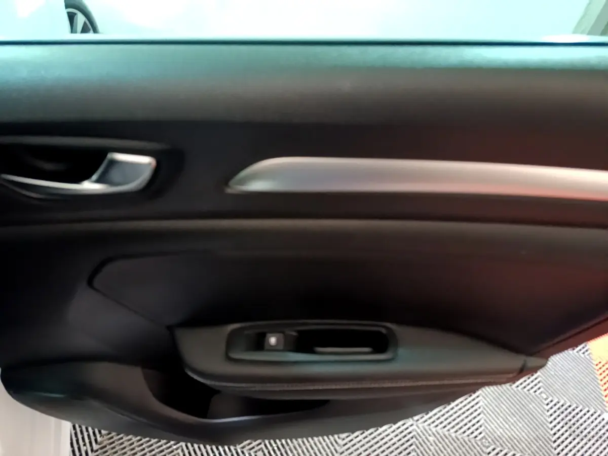 Gros plan sur la porte intérieure côté gauche de la Renault Mégane blanche, avec poignée argentée et commande de vitre noire.