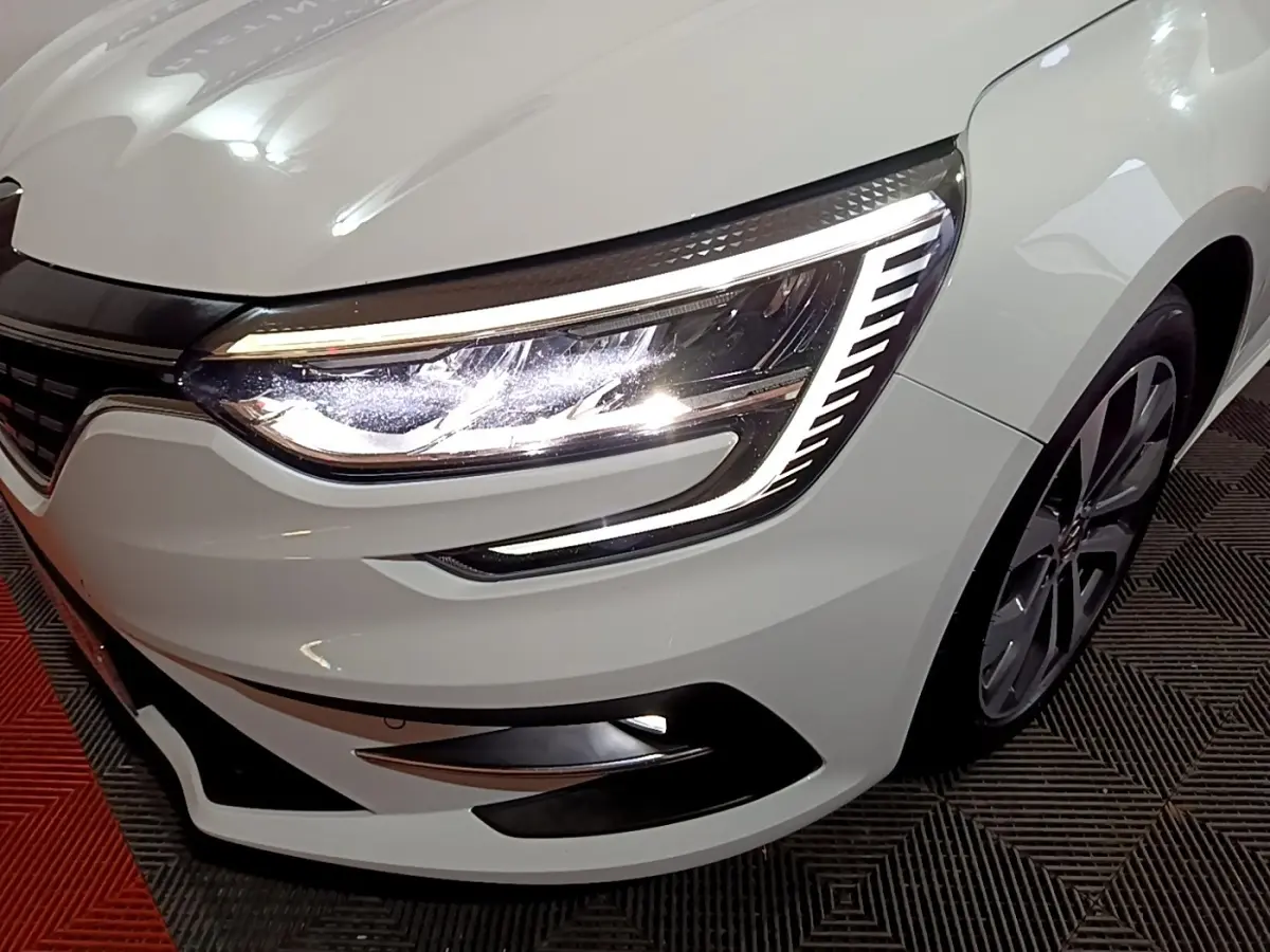Gros plan sur l’avant droit blanc de la Renault Mégane 2023, mettant en valeur son phare LED au design distinctif.