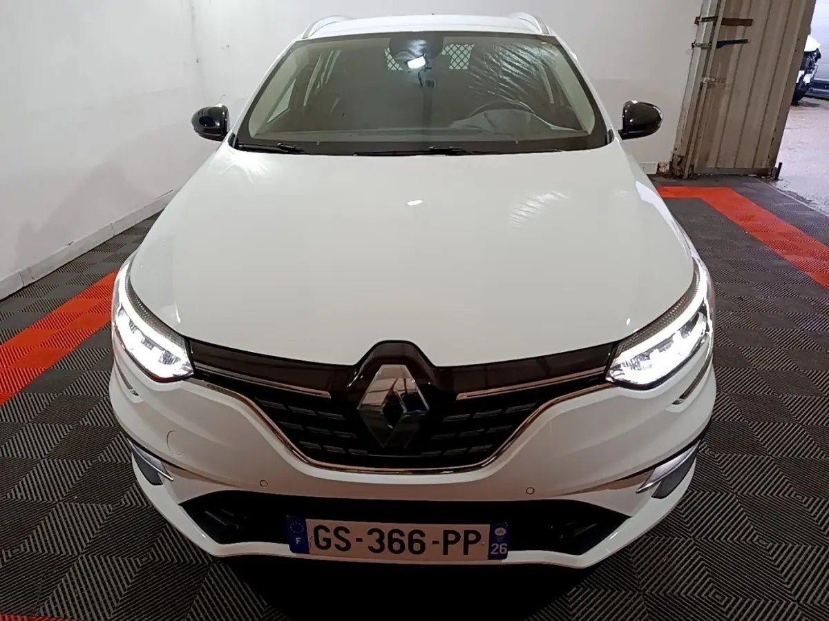 Vue avant d'une Renault Mégane Techno TCe 140 blanche avec phares LED allumés dans un garage.
