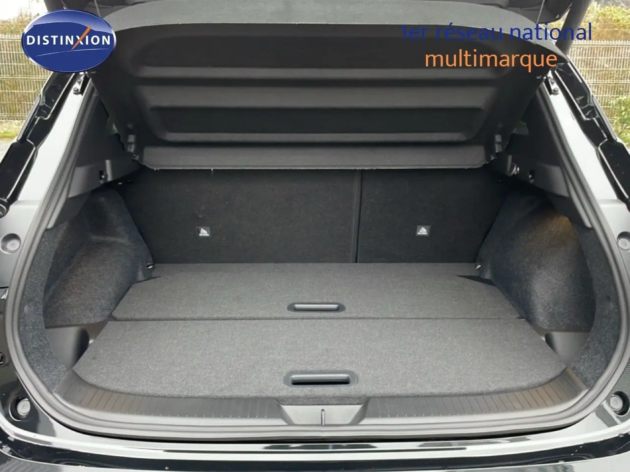 Coffre ouvert vu de l'arrière d'un Nissan Qashqai noir perle métal, plancher de coffre plat et tapis gris.