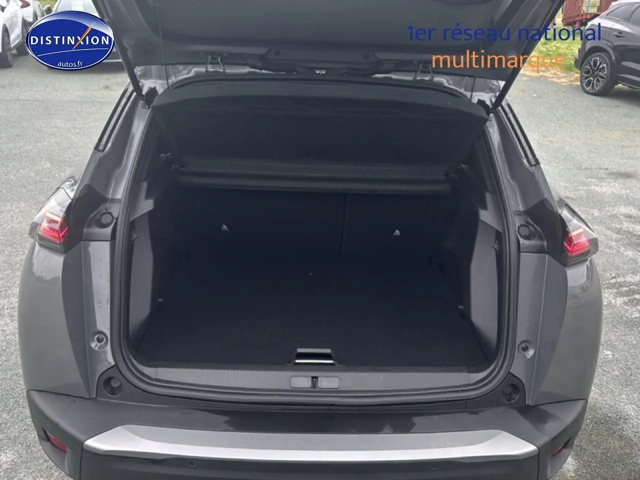 Coffre ouvert à l’arrière d’un Peugeot 2008 gris sélénite, montrant l’espace de chargement vide et les feux arrière LED allumés.