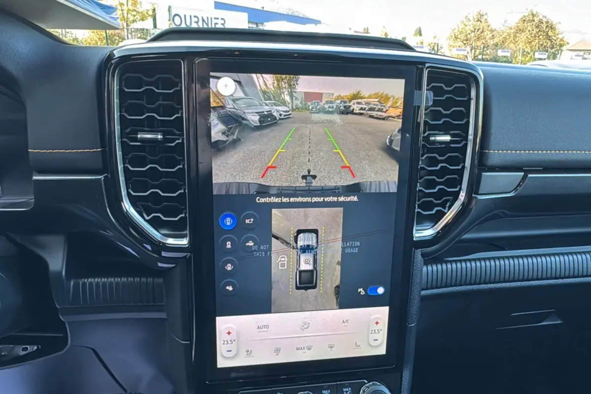 Vue intérieure centrée sur l'écran tactile du Ford Ranger PHEV 281 Wildtrak, affichant la caméra de recul et la climatisation.