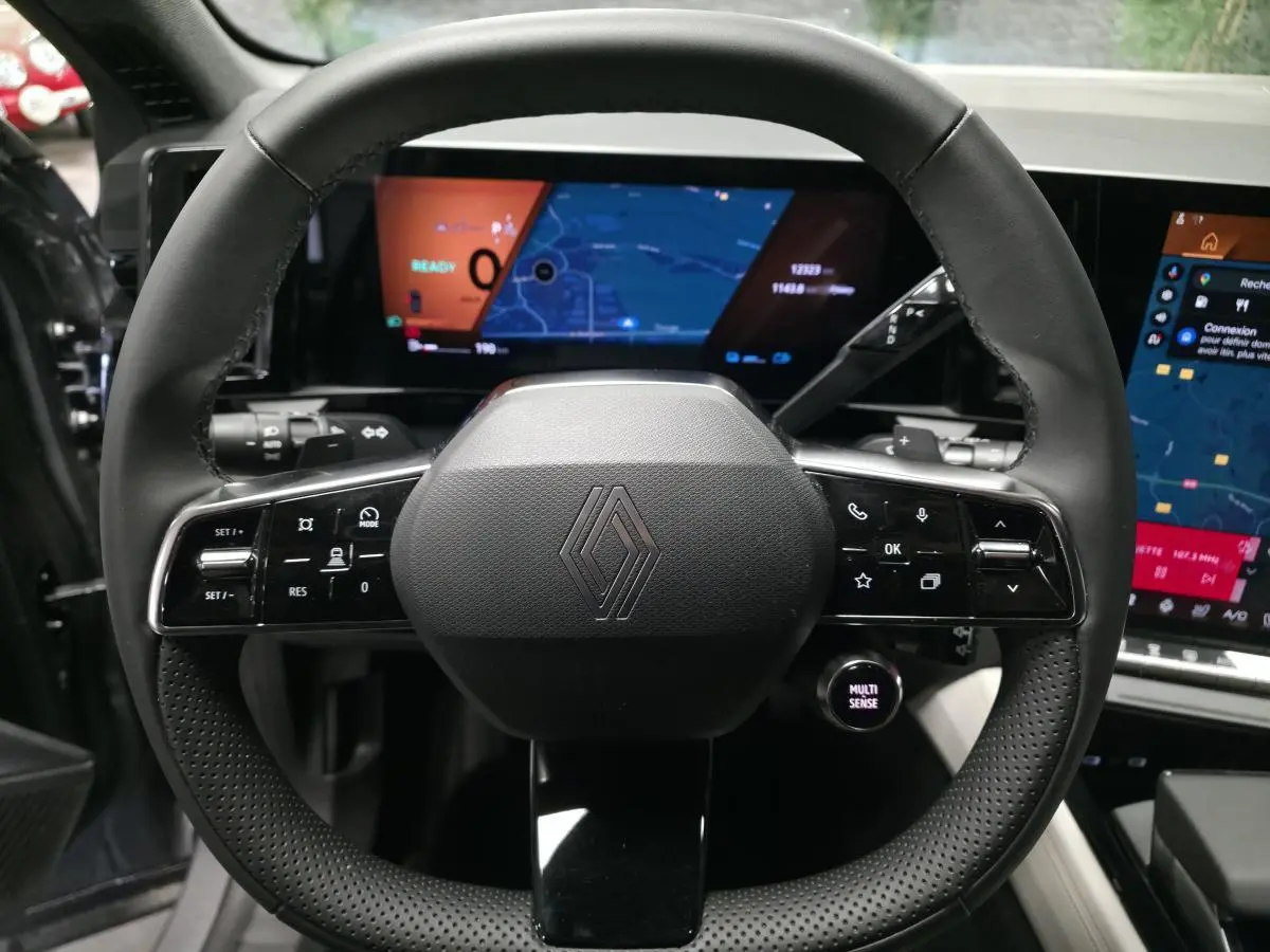 Volant noir perforé de Renault Espace 2025 avec commandes intégrées et écrans numériques en arrière-plan.