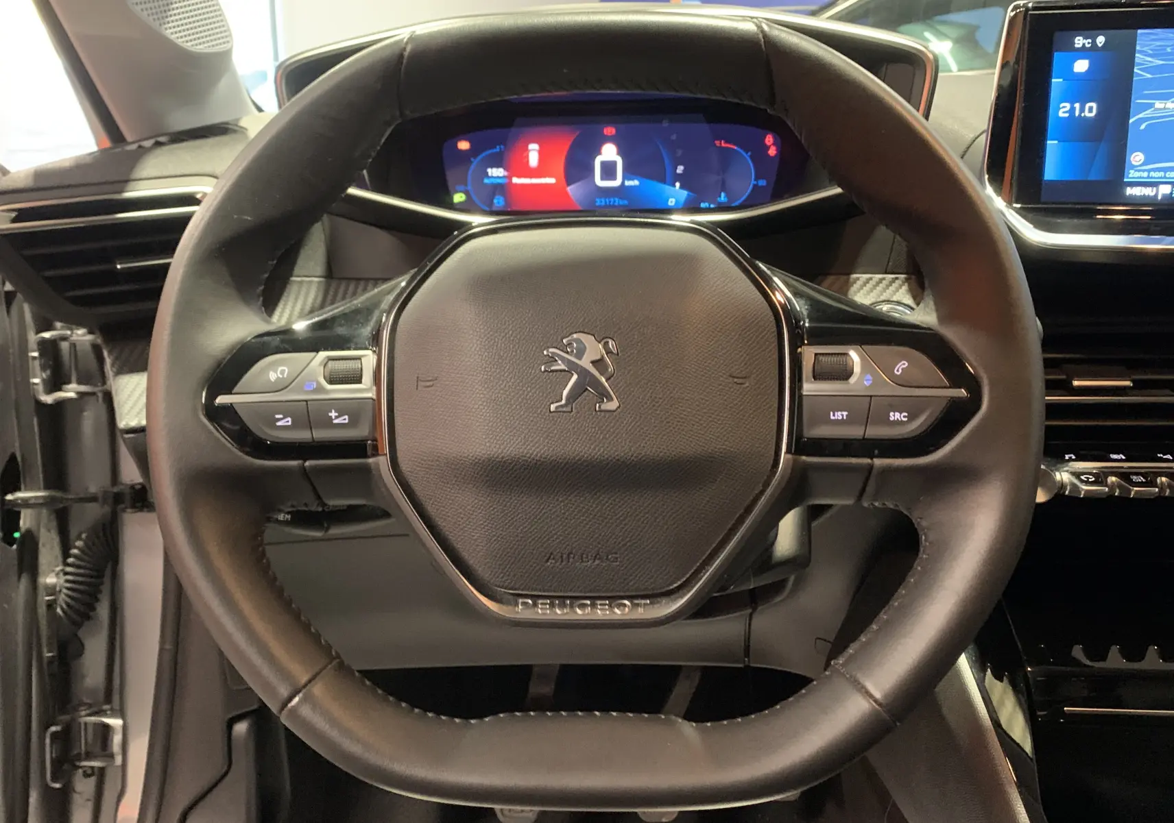 Vue rapprochée du volant noir de la Peugeot 208 PureTech 100 Allure Business avec tableau de bord numérique et écran GPS.