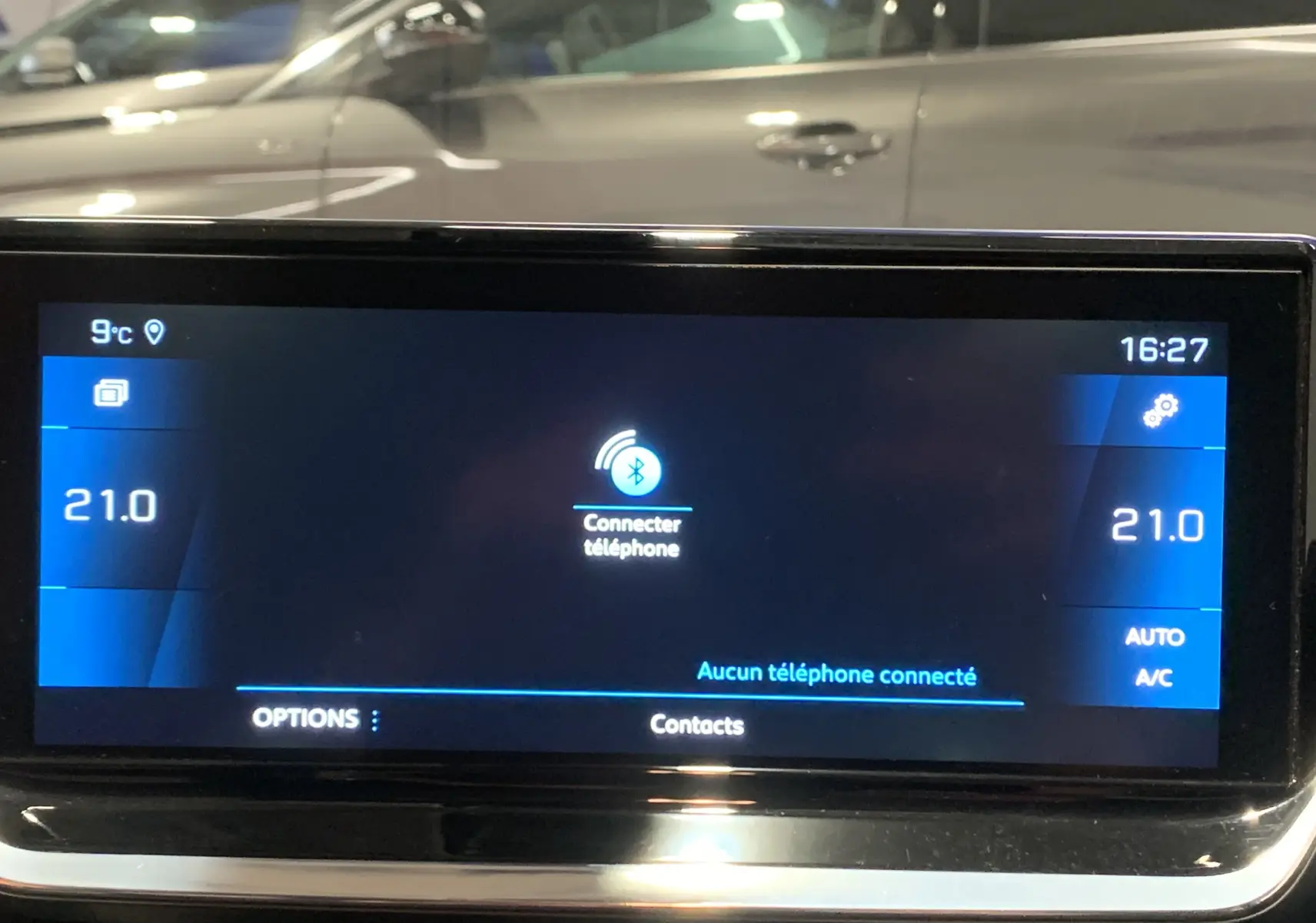 Écran tactile central de la Peugeot 208 gris, affichant la connexion Bluetooth et la température à 21°C, vue de face.