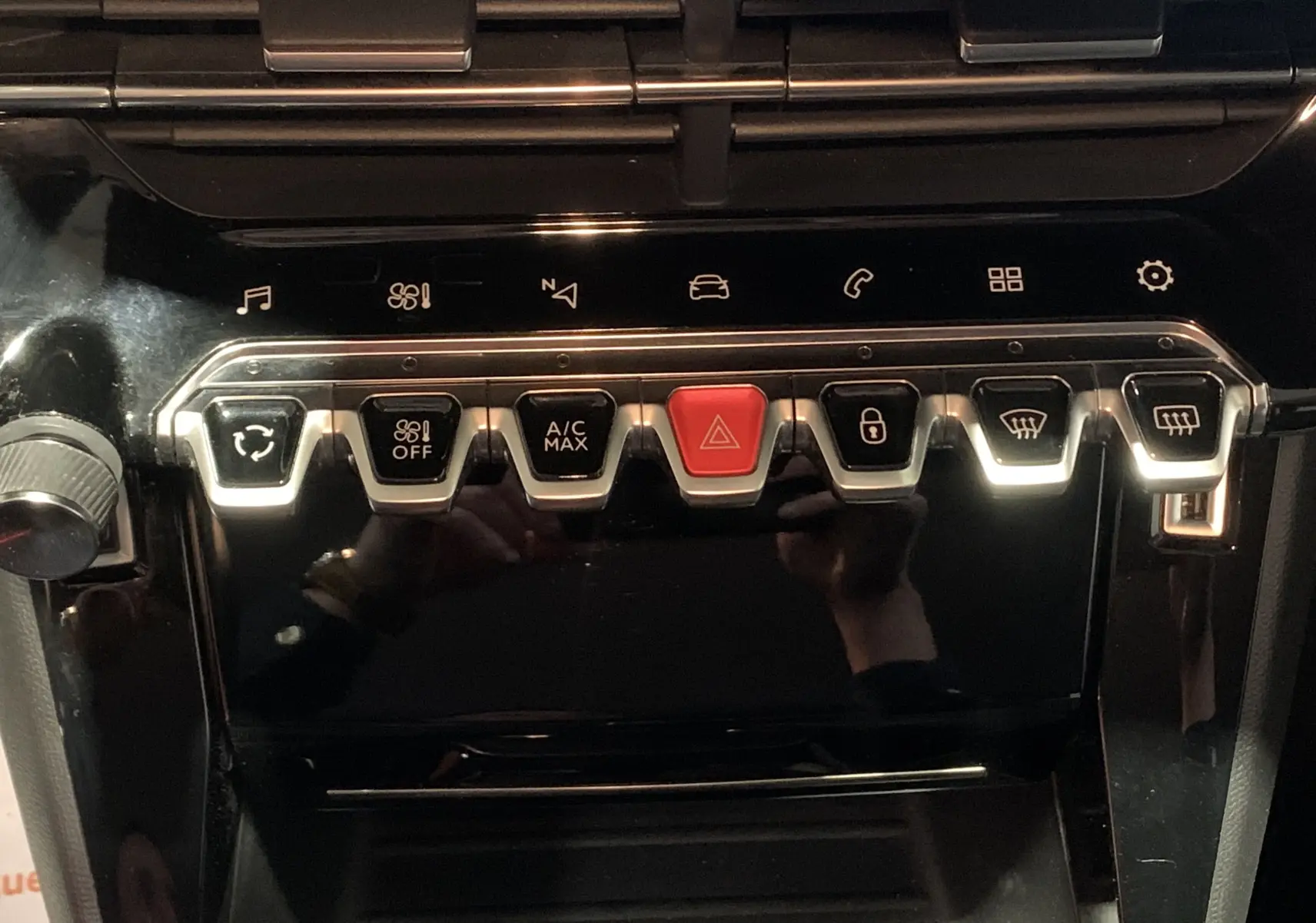 Gros plan sur la rangée de boutons de commande du tableau de bord noir brillant de la Peugeot 208 gris, version PureTech 100 Allure Business.