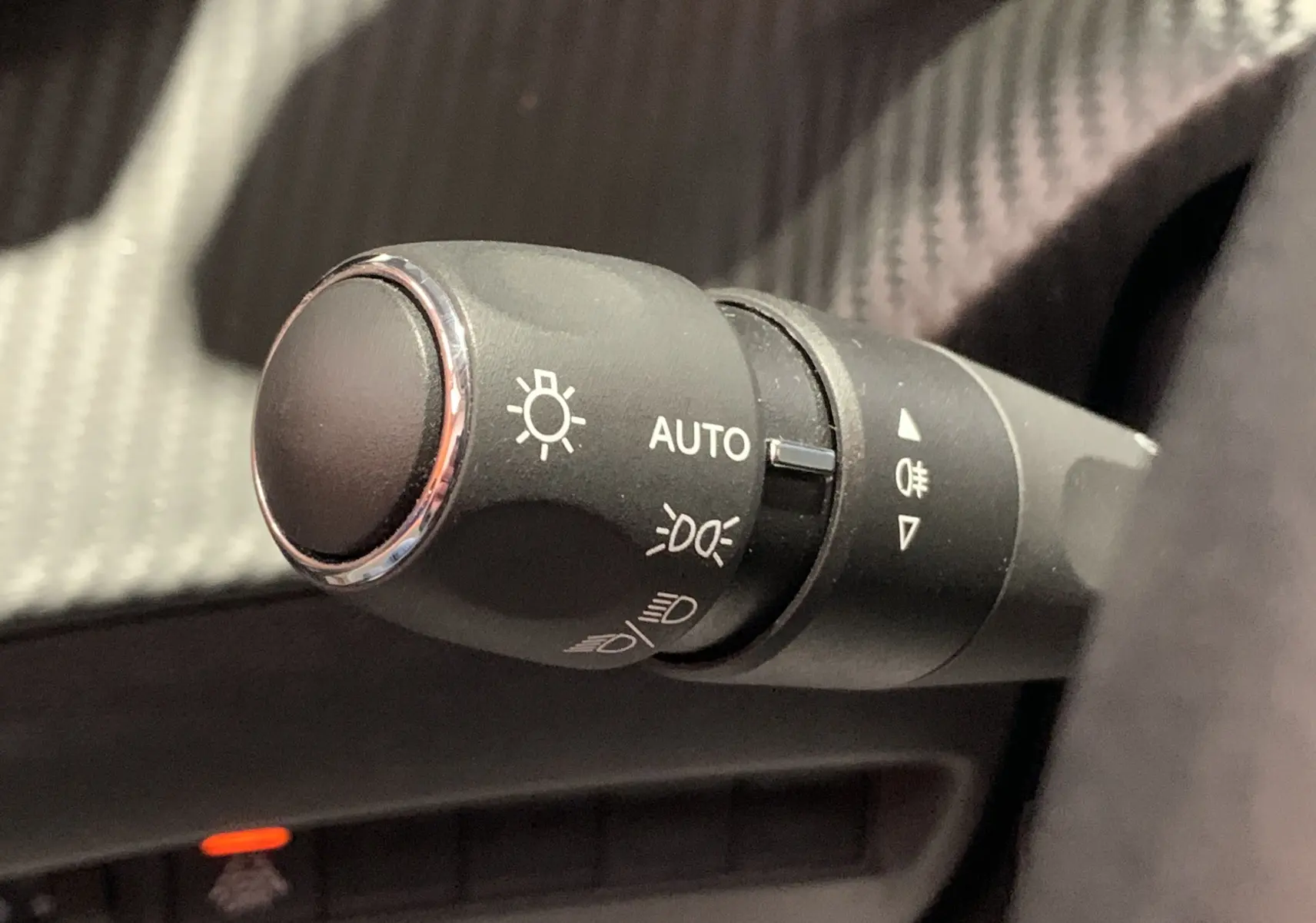 Gros plan sur la commande des phares noirs avec réglage automatique dans l’habitacle d’une Peugeot 208 gris 2021.