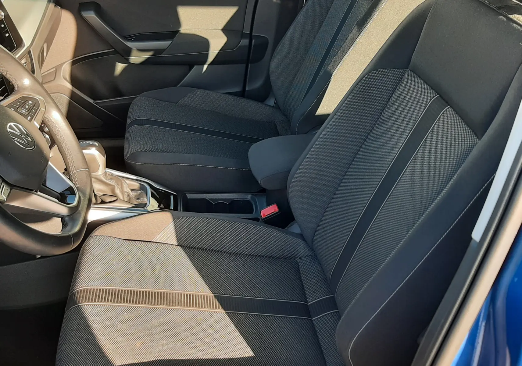 Vue intérieure côté conducteur du Volkswagen T-Roc bleu 2022, mettant en valeur les sièges en tissu gris foncé et la console centrale.