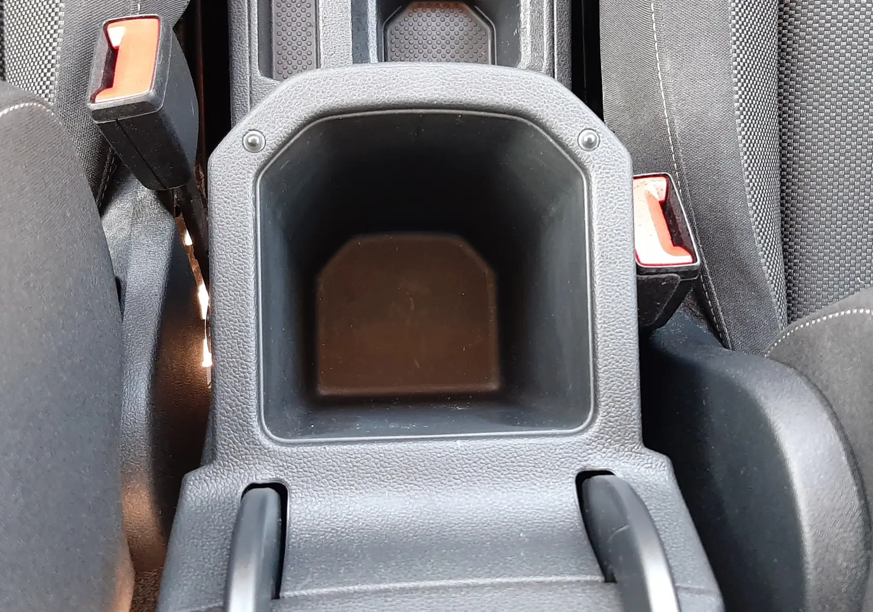 Vue plongeante sur le rangement central noir entre les sièges avant du Volkswagen T-Roc bleu 2022, avec ceintures de sécurité visibles.