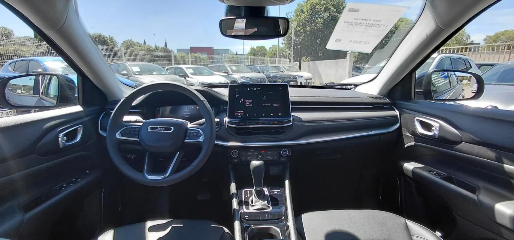 Vue intérieure avant du Jeep Compass 2025 bleu, montrant le volant, écran tactile central et levier de boîte automatique.