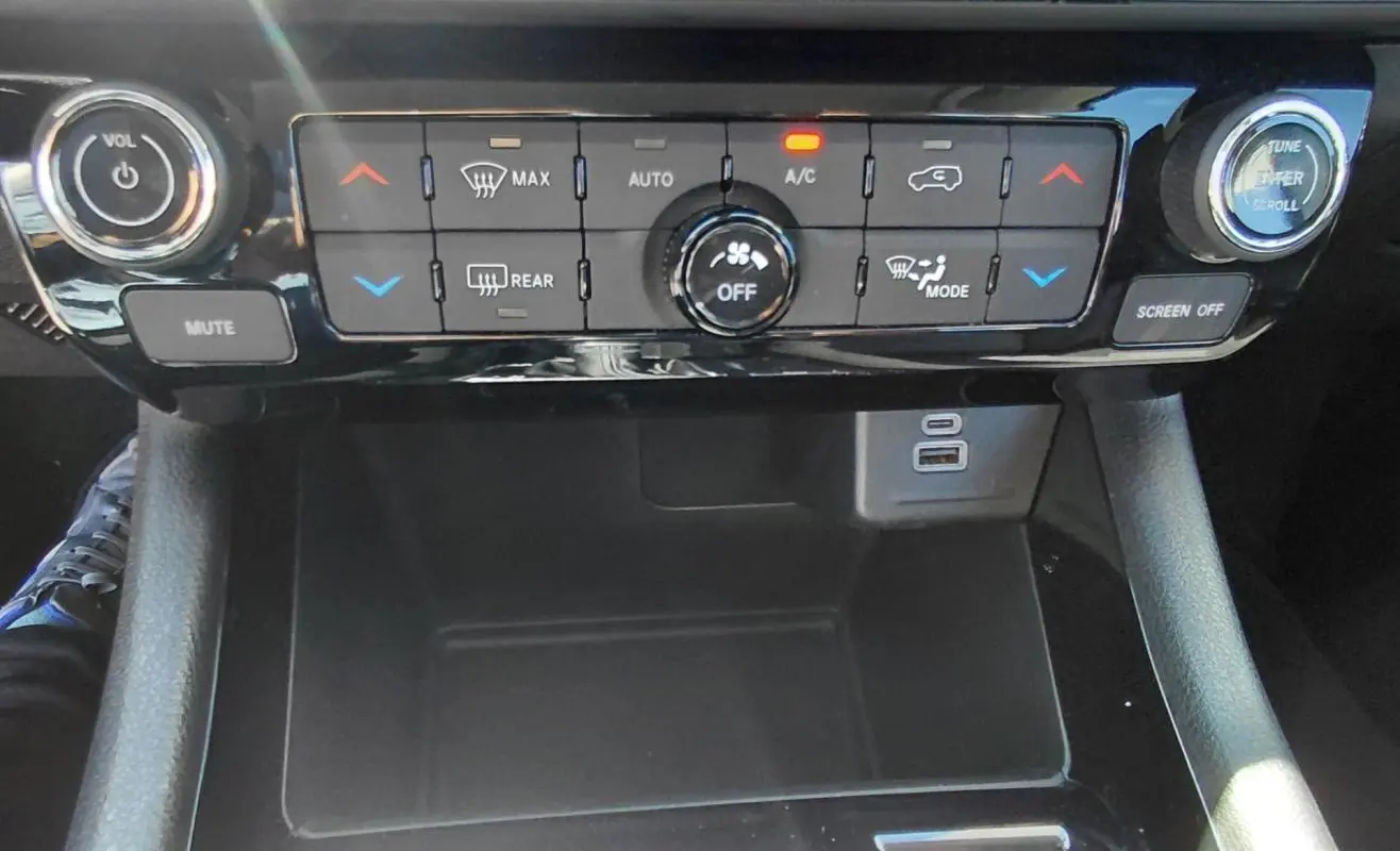 Vue rapprochée du tableau de bord et de la console centrale noire du Jeep Compass 2025, avec commandes climatisation et ports USB visibles.