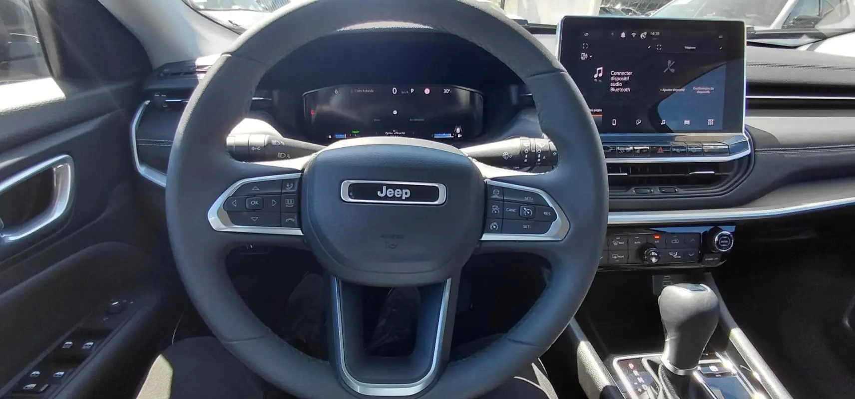 Vue intérieure centrée sur le volant Jeep et le tableau de bord avec écran tactile et levier de vitesse.