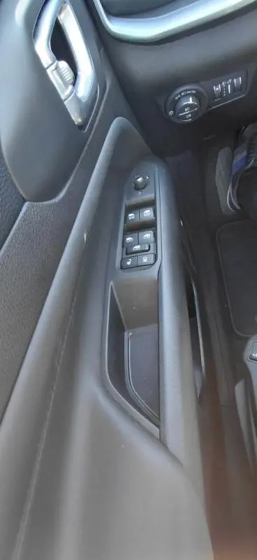 Vue rapprochée du panneau de porte côté conducteur du Jeep Compass bleu 2025, avec commandes électriques et réglage des phares.